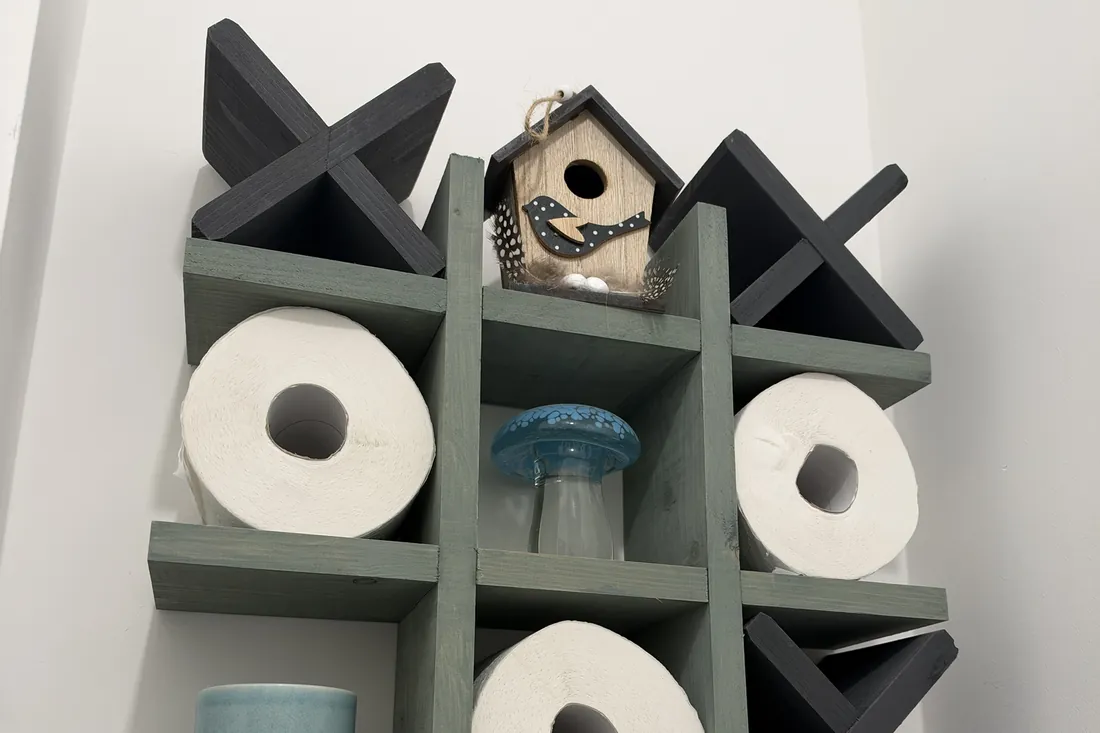 Handmade sage and charcoal noughts and crosses wall shelf holding toilet rolls, a birdhouse and a glass mushroom